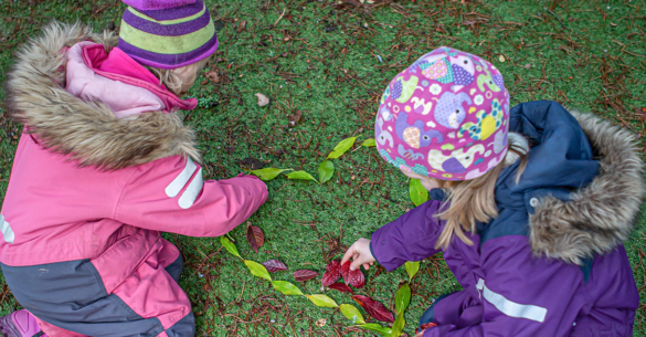 To jenter lager kunst av naturmaterialer. Her lager de et hjerte med blader.